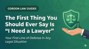 A featured image on a teal green background with the title "The First Thing You Should Ever Say Is 'I Need a Lawyer'." The graphic features a hand holding a glowing shield containing the scales of justice, symbolizing immediate legal protection and rights.